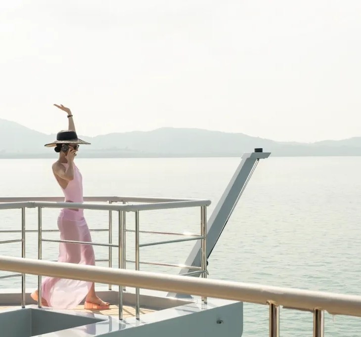 still from white lotus 3 - young woman on the edge of a yacht with her hand raised in the air, sea in the background