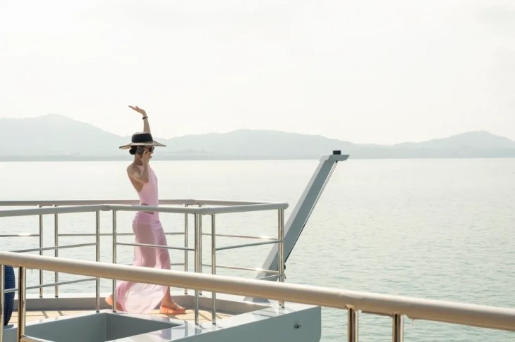 still from white lotus 3 - young woman on the edge of a yacht with her hand raised in the air, sea in the background