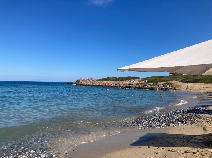 image of a beach in Crete with part of a beach umbrella to the right